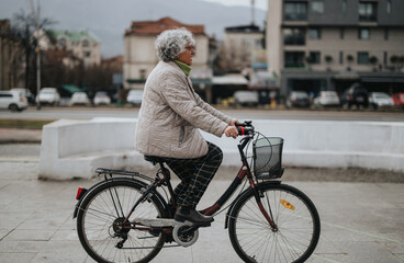 A mature woman with gray hair is cycling on a city street, demonstrating sustainable transport and active aging.