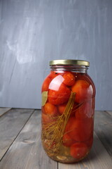 Canned food. Salted tomatoes in a glass jar on a gray background with space for text copyspace vertical photo