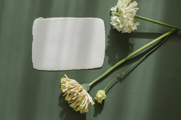 Overhead view of a blank handmade deckle edge card on a table with lisianthus, gerbera and ranunculus flowers in sunlight