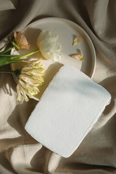 Overhead view of a Blank piece of homemade card on a ceramic plate with gerbera, tulip and ranunculus flowers