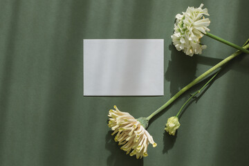Overhead view of a blank card on a table with lisianthus, gerbera and ranunculus flowers in sunlight