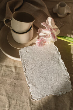 Overhead view of blank piece of homemade deckle edge card with a parrot tulip and assorted ceramics on a table