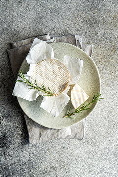 Overhead view of a whole brie with fresh rosemary on a plate with cheese knives