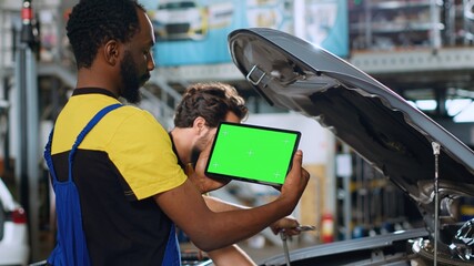 Mechanic using green screen tablet in car service to watch tutorial on how to fix unknown problem. Employee using chroma key device to look online for video showing how to repair broken vehicle part - obrazy, fototapety, plakaty