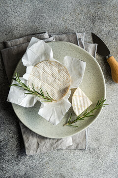 Overhead view of a whole brie with fresh rosemary on a plate and folded napkin