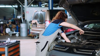 Diligent mechanic in garage using torque wrench to tighten studs inside opened up vehicle after changing oil. Auto repair shop employee doing maintenance on car, wiping leftover mess
