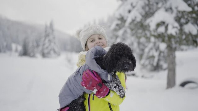 Little girl holds poodle dog in her arms in the snow