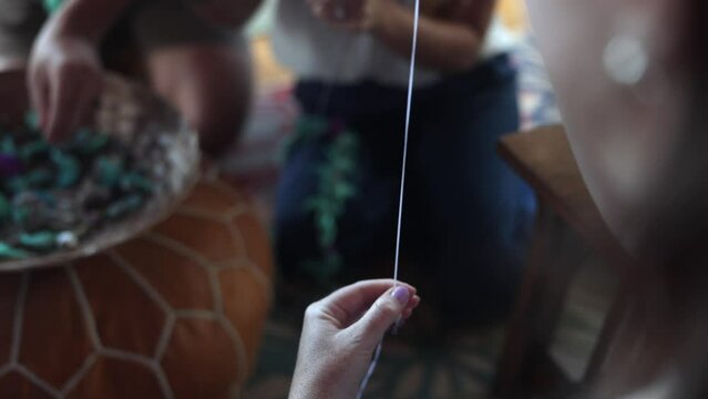 Close-up of a woman making lei in Hawaii, plumeria flowers garland crown handmade.