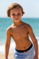 Cute little boy playing on the beach on summer holidays. Joyful child in nature with beautiful sea, sand and blue sky. Happy kid on vacations at seaside running in the water and having fun