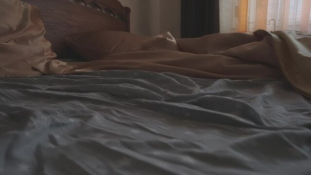 Cinematic closeup of unmade bed with crumpled sheets and pillows symbolizing restlessness and lack of sleep. Dawn light has muted color