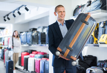 Portrait of man picking new big plastic luggage bag with wheels in shop