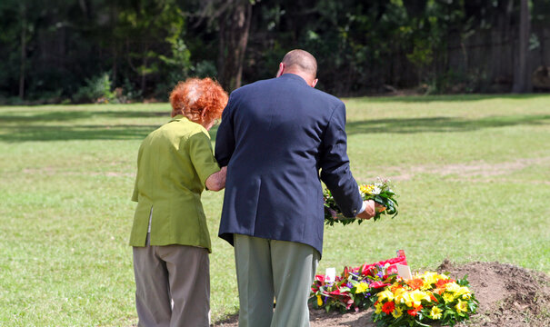 An old lady supported by a military veteran lay remembrance flowers during ANZAC Day
