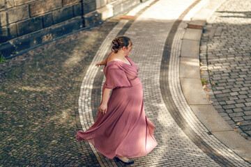 A young plus size woman wearing a pink dress dancing in the street of a city. Body positivity concept