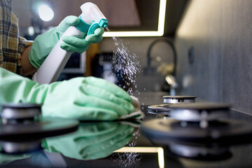 Hand in a green rubber glove washes the gas stove. Cleaning the kitchen