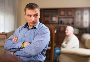 Portrait of upset adult man sitting at home table, having problems in relationship with his aged...