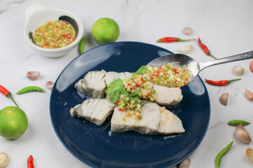 Boiled fish with dipping spicy sauce in blue plate on white table. Seafood. Asian thai street food.