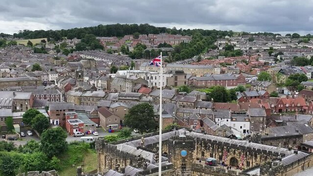 Aerial View of British Flag Waving on Pole Above Alnwick Medieval Castle and Town, England UK