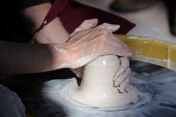 Hands of a ceramic artist shaping a clay vessel on a pottery wheel, demonstrating centering and forming techniques used in traditional wheel-thrown pottery and hands-on craft production