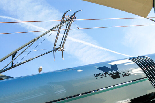 Detail view of Valley Metro Rail pantograph and overhead electric wires against a blue sky, highlighting Phoenix-area public transportation infrastructure