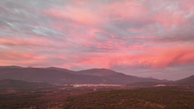 Side drone flight over a valley surrounded by mountains and in which there are several towns at sunset time with pinkish orange and violet clouds in Avila Spain