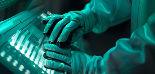 Detailed shot of space gloves pressing buttons on a scientific instrument that emits teal light...