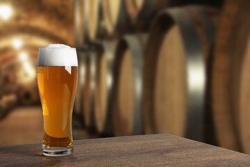 Glass with fresh beer on wooden table in cellar, space for text