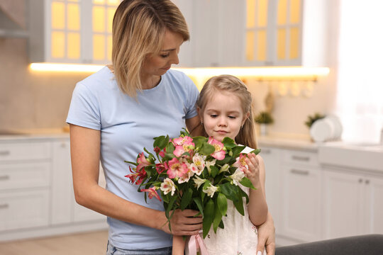 Little daughter congratulating her mom with bouquet of alstroemeria flowers in kitchen. Happy Mother's Day