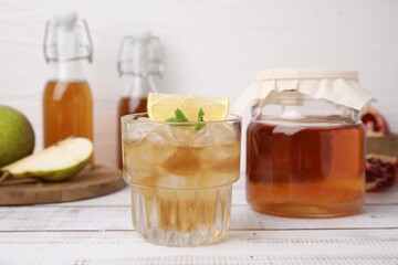 Tasty kombucha and ice cubes in glass on white wooden table