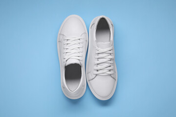 Pair of stylish white sneakers on light blue background, top view