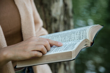 Close-up hand a woman sitting outside reading the Bible and worshiping God. natural background in the garden.