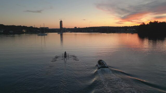 Cinematic drone shot of a Sport canoe with a crew of four paddling through calm waters in an Atlantic Ocean bay at sunset in Halifax, Canada. Rowing athletes train in the evening at dusk at sunset.