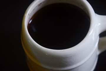 Closeup photo of Black coffee in white and yellow cup on black ceramic table