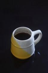 Black coffee in a white and yellow cup on a black ceramic table