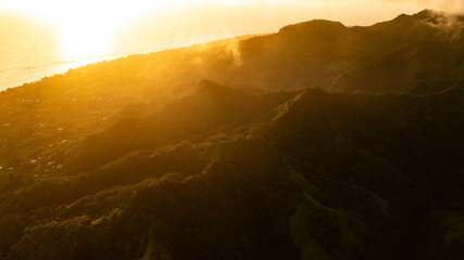 A warm golden sunshine glow saturates the natural rugged slopes of Rarotonga's mountain range.