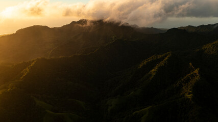 A golden wash of sunshine invades one half of the Rarotongan island mountain range.