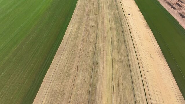 AERIAL: Irrigation tubes and sprinklers run along a strip of unharvested turf at a grass farm. Watering system runs along a strip of soil primed for sod cultivation. Flying above a massive grass farm.