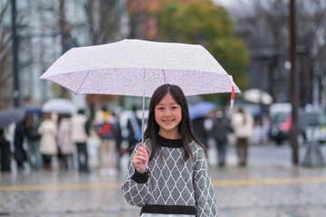 傘を差して原宿の街を歩く小学生の女の子