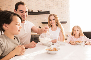 Happy family sitting at the table and eating breakfast - 761059198