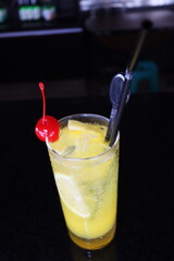 a glass of cold and fresh healthty yellow orange juice with a cherry fruit