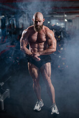 Muscular bald man posing in shorts. Bodybuilder showing off his shape in the gym. 