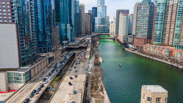  An aerial drone  view of a bustling Chicago metropolis The cityscape is reflected in the serene waters of a green-tinted river. Cars stream along the adjacent highway
