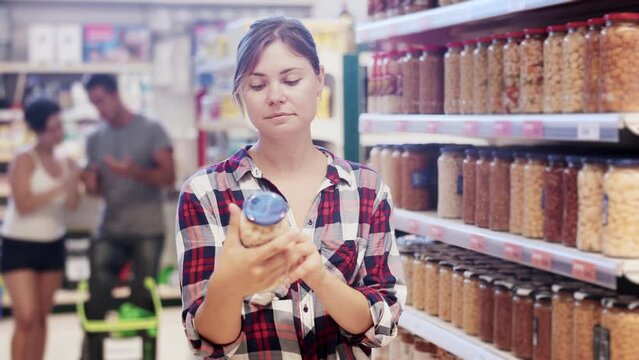 Woman standing at shelf in grocery store and selecting pickled products.