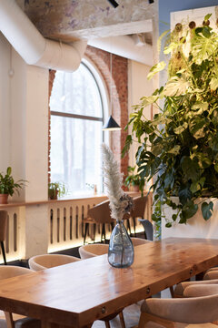 Vertical no people shot of part of modern restaurant interior with flowers in glass vase on wooden table, copy space
