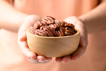 Raw peeled pecan nuts in wooden bowl holding by woman hand, Food ingredient