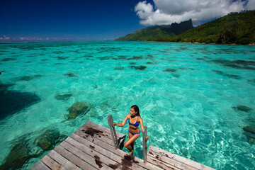 Luxury beach travel vacation woman in Tahiti overwater bungalow hotel villa swimming. This image is...