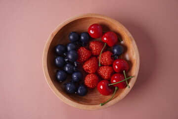 berries in a wooden bowl on isolated pink background table
