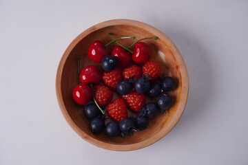 berries in a wooden plate on isolated white background table