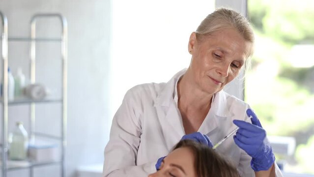 Young female patient lying on clinical chair undergoing hair care procedure by injection method 