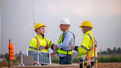 Engineers and manager wearing uniform holding solar call panel work cooperate hand teamwork in wind...
