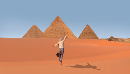 Muslim woman in gray trousers and a scarf jumps on the sands of the Sahara desert -  Giza Pyramid Complex at amazing sunset - Cairo, Egypt 